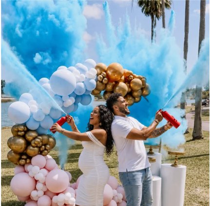 Gender reveal moment with blue smoke, gold and pastel balloon installation